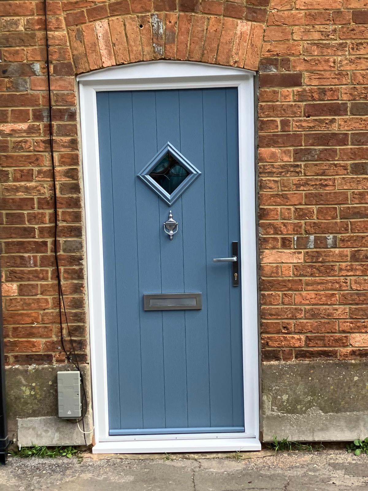 Blue composite front door with chrome door furniture in a brick wall
